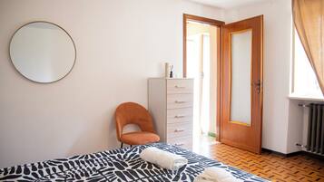 Quarto com cama, uma cadeira, cômoda e porta que dá para outro espaço.