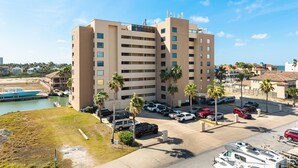 A multi-story hotel with a parking lot, several parked cars, and a body of water in the background. - Cute Bayside Studio #43 (South Padre Island)