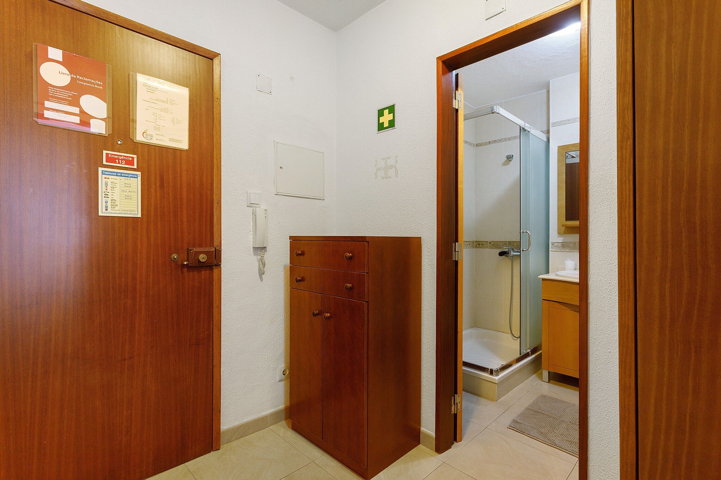 Puerta de madera con información de contacto de emergencia, un armario pequeño y una zona de ducha visible a través de una puerta abierta.