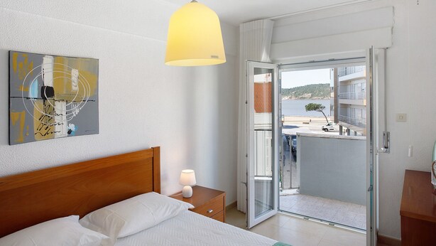 A bedroom with a bed, bedside table, lamp, artwork, and a balcony with a view. - Apartment 'Campo Mar - T1 Beach View' with Sea View, Balcony and Wi-Fi (São Martinho do Porto)