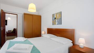 Un lit bien fait, avec du linge de lit et des serviettes blanches, une tête de lit en bois, une lampe de chevet et un tableau accroché au mur.