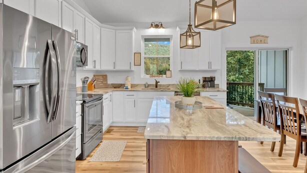 A modern kitchen with stainless steel appliances, a marble island, and a view of the outdoors. - Sleeps 10, HotTub, Game Room, Views, Pet Friendly (Sevierville)