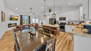 A modern kitchen with white cabinets, stainless steel appliances, and a wooden dining table. - Sleeps 10, HotTub, Game Room, Views, Pet Friendly (Sevierville)
