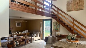 Um amplo loft com escada de madeira, área de jantar com mesa e cadeiras, e um canto aconchegante para sentar com almofadas e sofá.