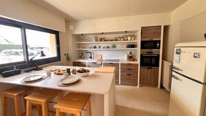 Uma cozinha compacta com uma ilha central, banquetas de madeira, um refrigerador e um micro-ondas.
