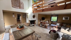 Uma sala de estar ampla com teto alto, lareira, um banco de madeira, sofá e mesa de jantar.