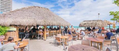 Un espace de restauration en plein air, agrémenté de parasols en chaume, de tables et de chaises en bois, et offrant une vue sur la plage.