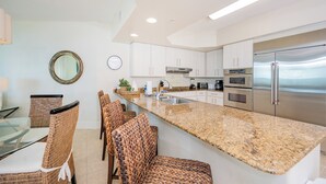 A modern kitchen with white cabinets, stainless steel appliances, a granite countertop, and wicker chairs.