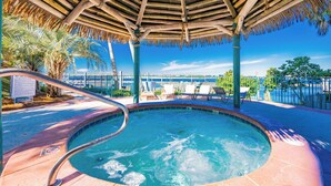 A hot tub area with a wooden canopy, lounge chairs, and a poolside view.