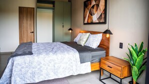 A bedroom with a bed, bedside table, nightstand, and a potted plant.