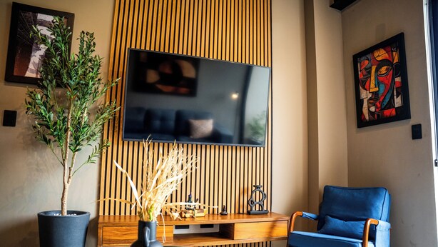 A modern living room with a TV, a blue chair, a wooden cabinet, and a potted plant.
