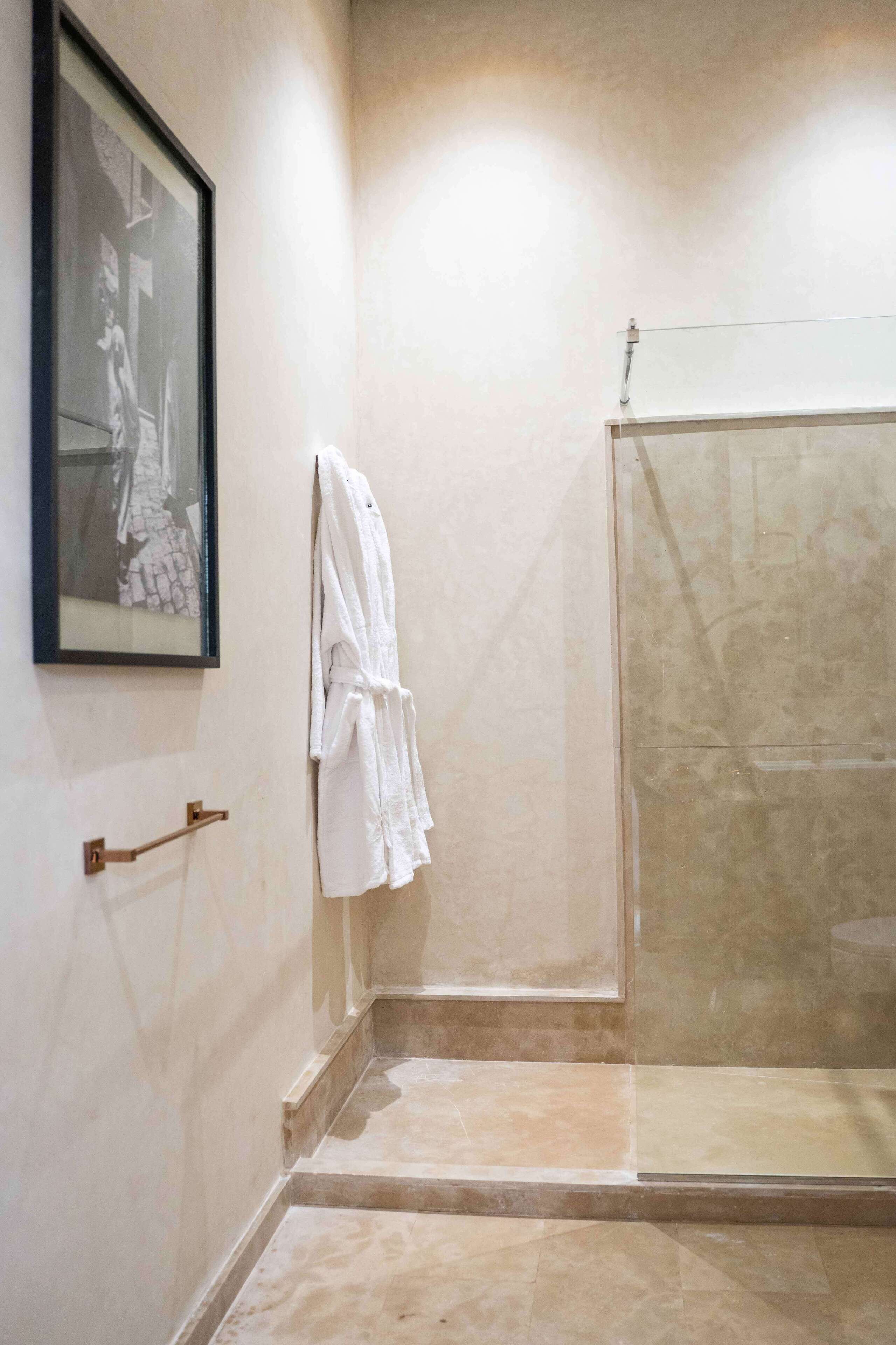 A bathroom with a glass shower enclosure, a framed picture on the wall, and a towel rack with white towels.