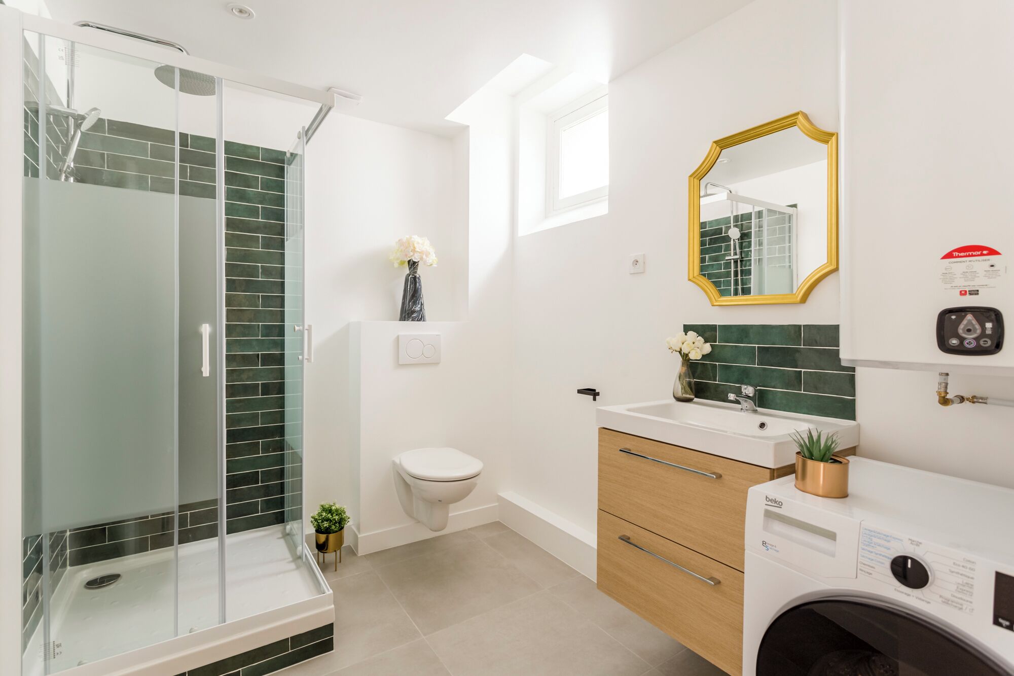 A modern bathroom with a glass shower enclosure, a toilet, a sink with a mirror, and a washing machine.