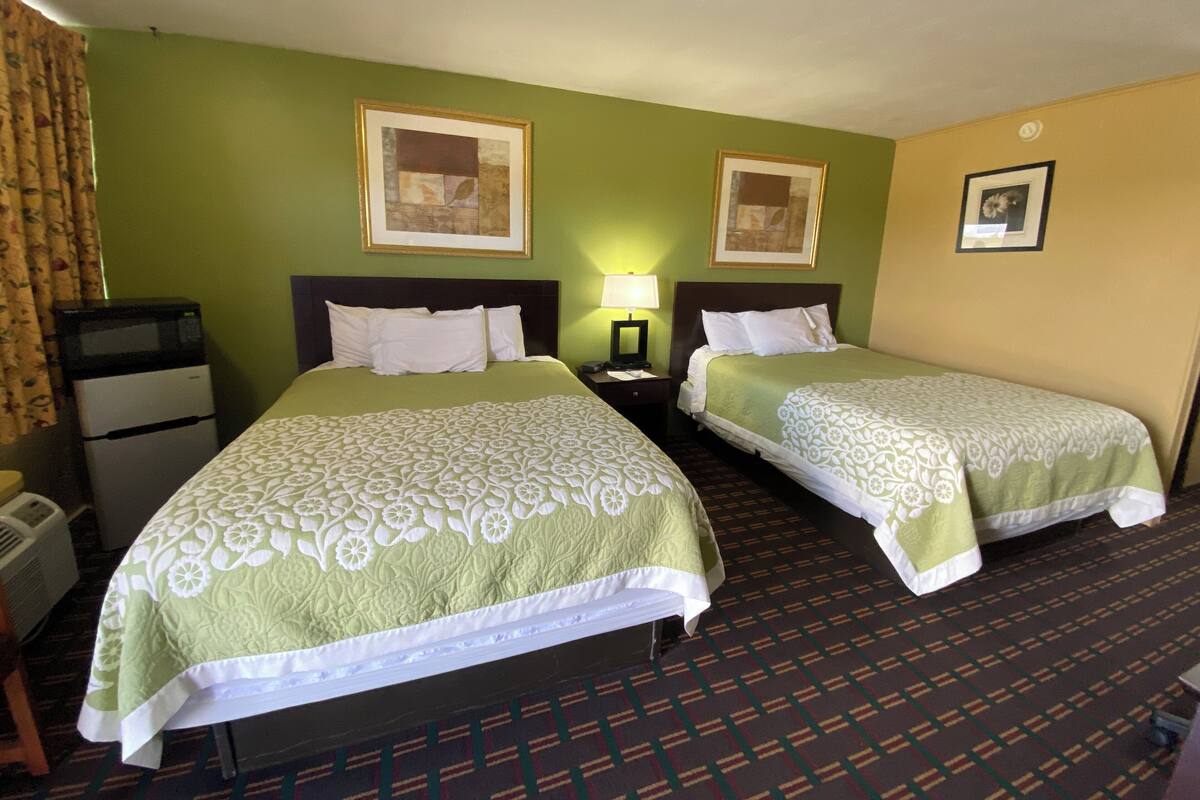 Une chambre d’hôtel avec deux lits, une petite kitchenette et une table de chevet avec une lampe.