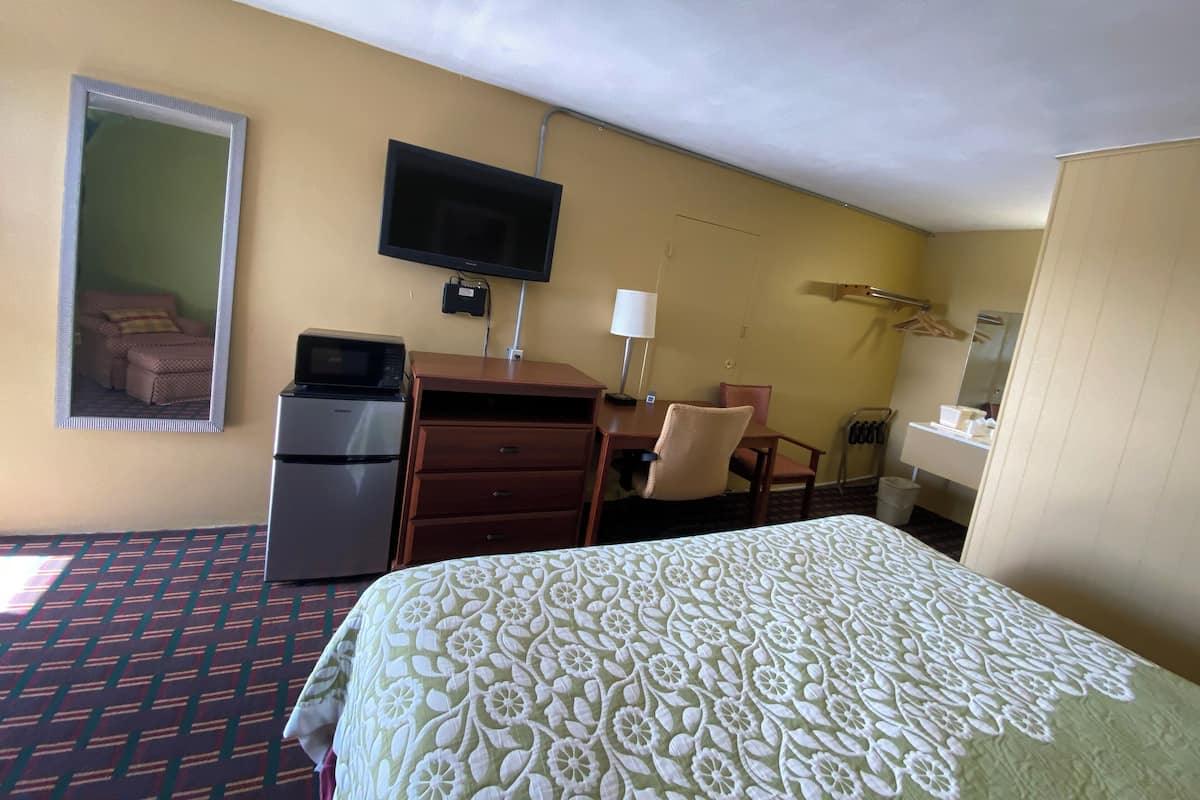 Une chambre d’hôtel équipée d’un lit, d’un bureau avec un ordinateur, d’une télévision, d’un four à micro-ondes et d’un petit réfrigérateur.