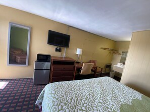 A hotel room with a bed, a desk with a computer, a television, a microwave, and a small refrigerator.