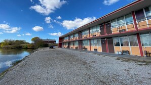 A motel with a gravel driveway, a river in the background, and a clear blue sky. - Innkeeper Motel (Hamel)