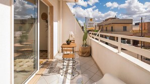 Ein Balkon mit Holztisch und -stühlen, einem Blumentopf und Blick auf die Stadt.