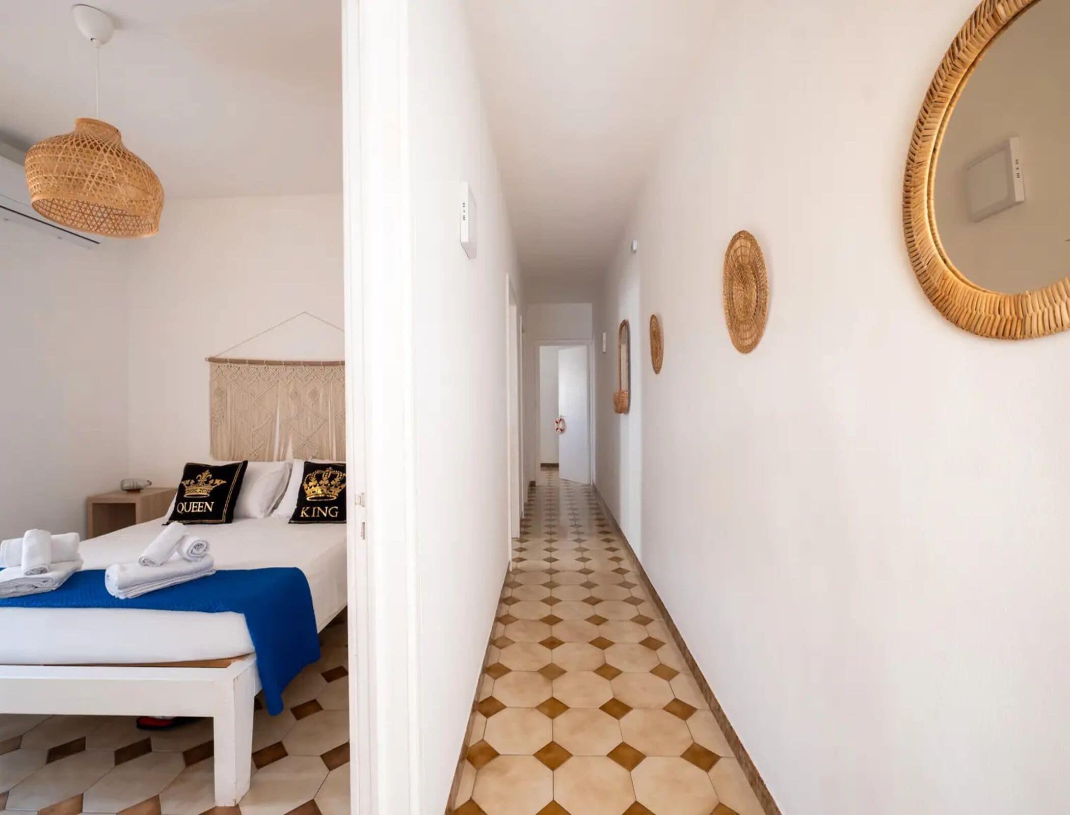 Een hotelkamer met een bed, een nachtkastje, een spiegel en een gang met een vloer met patroon.