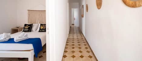 A hotel room with a bed, a bedside table, a mirror, and a hallway with a patterned floor.