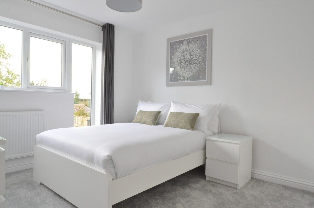 A bedroom with a large bed, a bedside table, a window, and a framed picture on the wall.