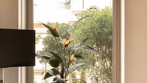 A living room with a large window, a flat-screen TV, a round wooden table, and a potted plant. - Montera Apartment with Pool (Bastia)