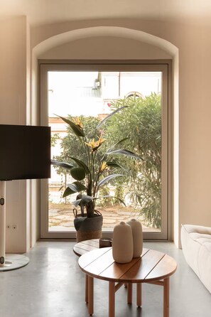 A living room with a large window, a flat-screen TV, a round wooden table, and a potted plant. - Montera Apartment with Pool (Bastia)