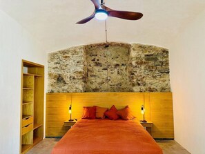 A bedroom with a stone wall, wooden bed frame, and two bedside lamps.