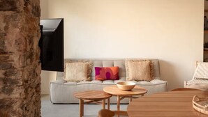 A living room with a grey sofa, two wooden side tables, and a television mounted on the wall. - Montera Apartment with Pool (Bastia)