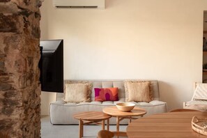 A living room with a grey sofa, two wooden side tables, and a television mounted on the wall.