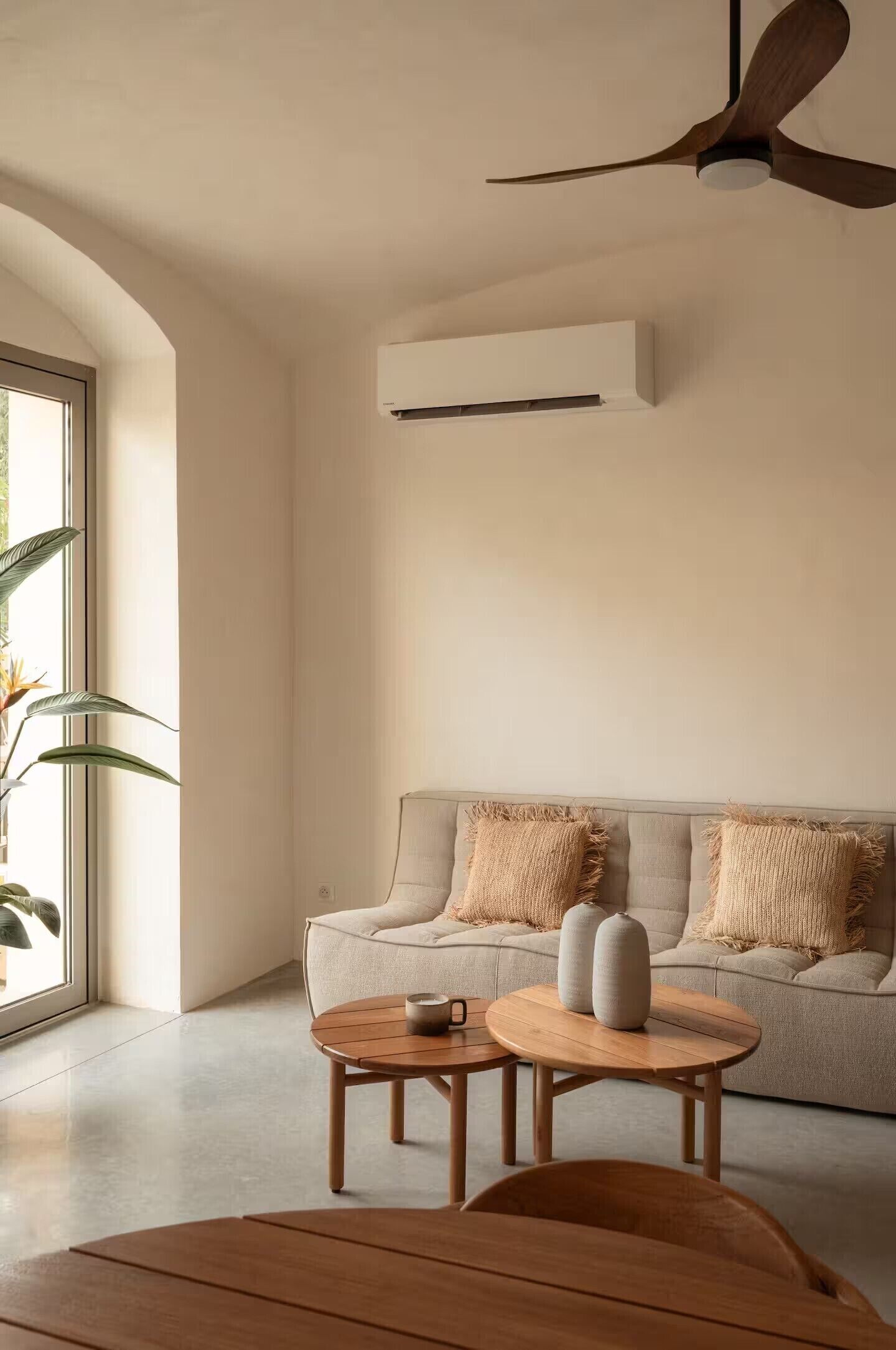Ein modernes Wohnzimmer mit einer Couch, zwei runden Holztischen und einem Deckenventilator.