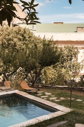 A swimming pool with a stone border, surrounded by grass and trees.
