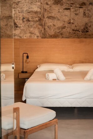 Una habitación de hotel con dos camas, cabecero de madera, lámpara de noche y una silla de madera.