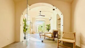 A spacious room with a large arched doorway leading to a balcony, a wooden chair, a small table, and a potted plant. - Montera Apartment with Pool (Bastia)