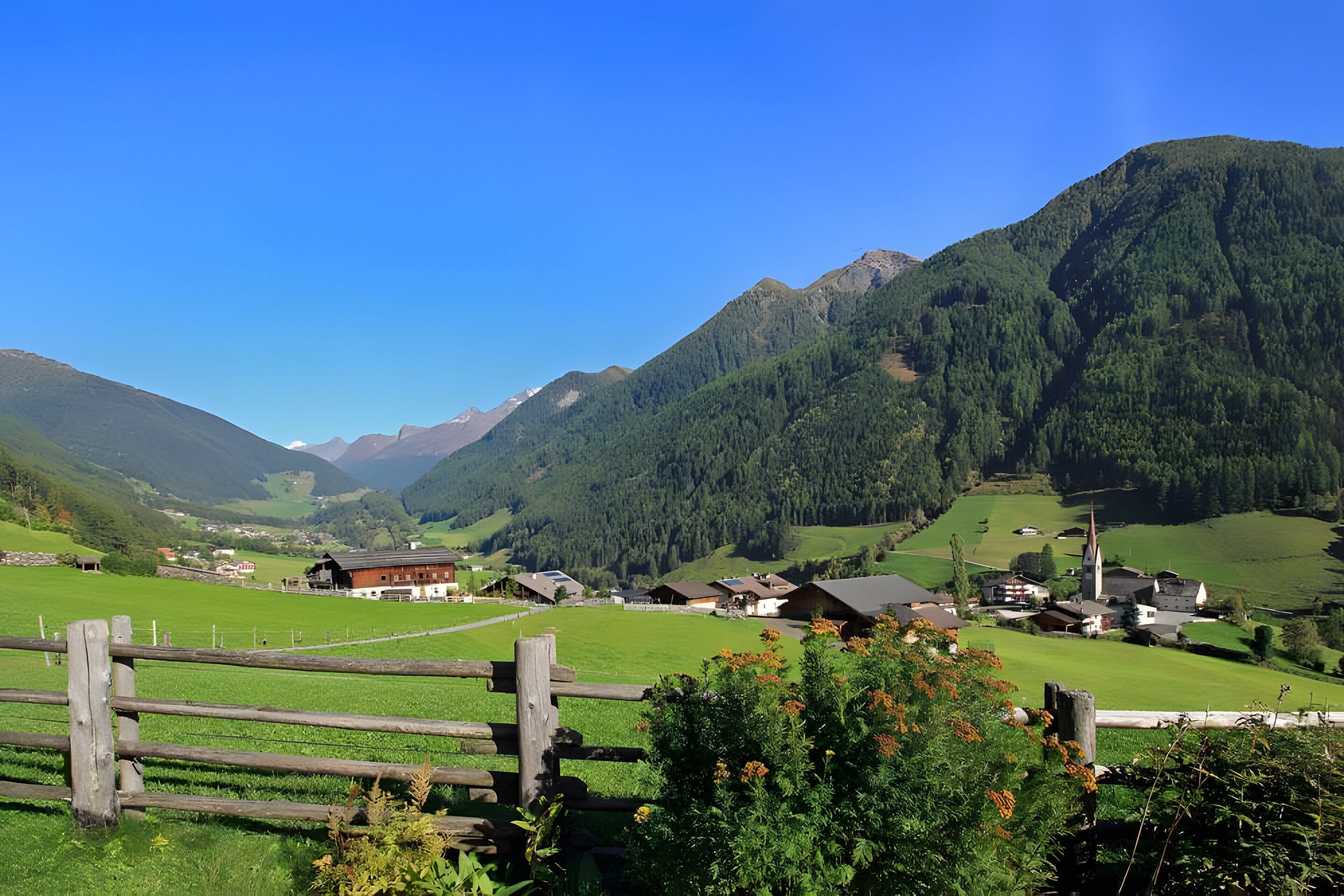 Ein ländliches Dorf mit Häusern, einer Kirche und Bergen im Hintergrund.