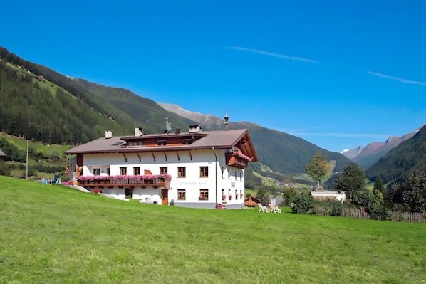 A white building with a red roof, balconies with flowers, and a mountain backdrop.