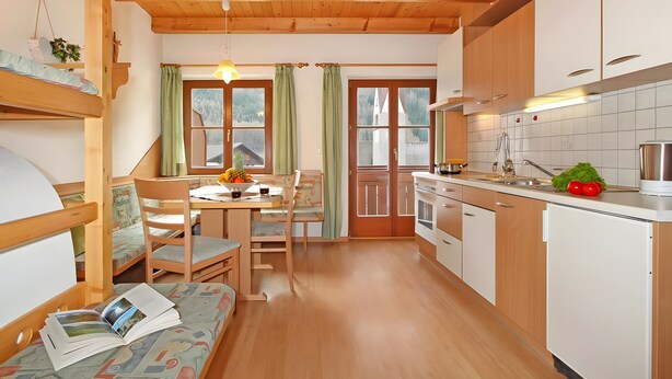A cozy kitchen with wooden cabinets, a dining table with chairs, and a window with curtains.