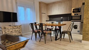 Cocina moderna con armarios de madera, una mesa de comedor con sillas, un televisor montado en la pared y una lavadora.