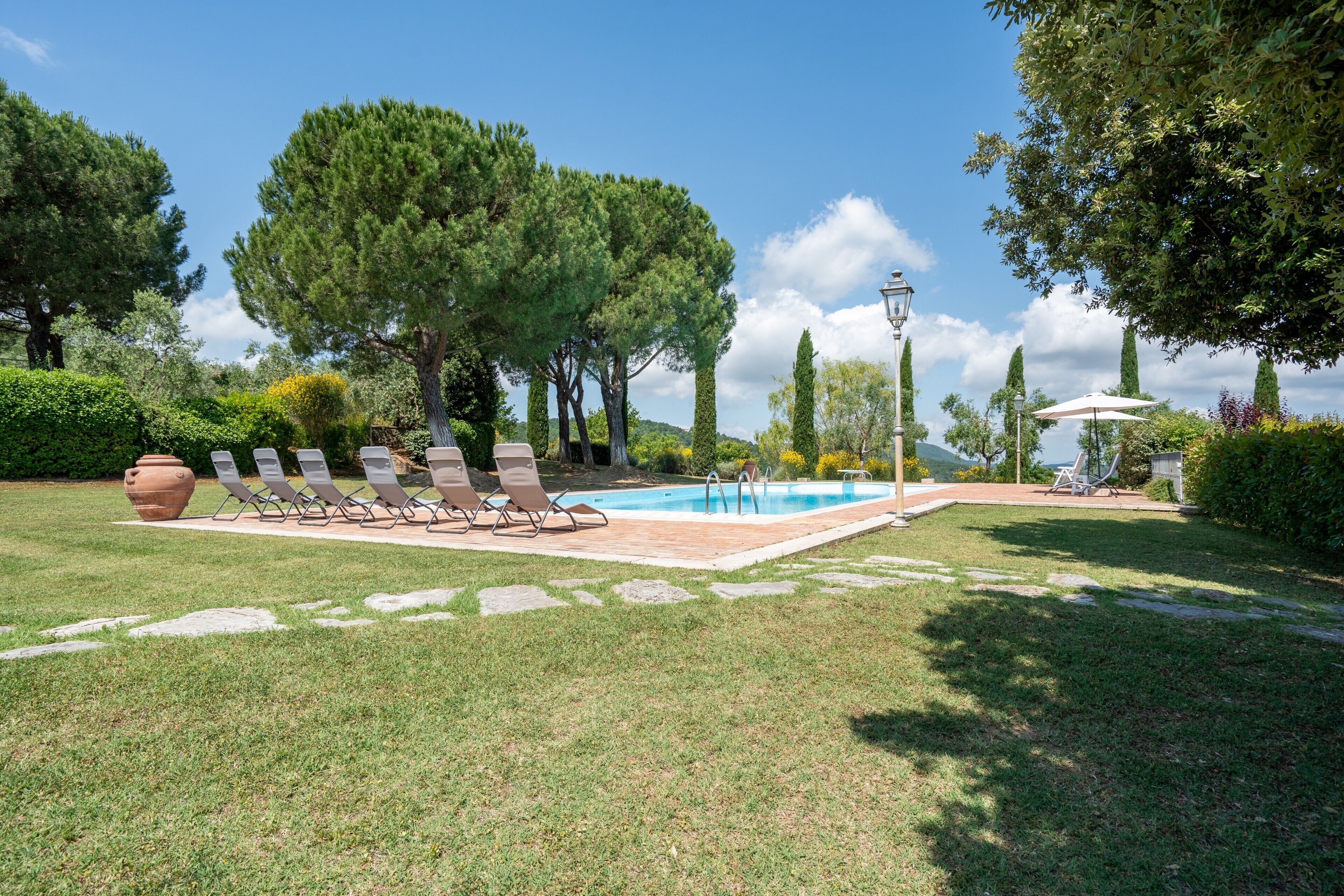 A pool area with lounge chairs, a pergola, and a lamp post.