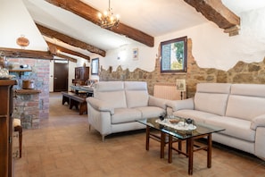 A cozy living room with a stone wall, wooden beams, a sofa, a glass coffee table, and a fireplace.