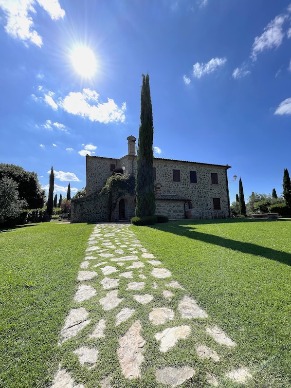 A stone building with a central courtyard, a tall cypress tree, and a clear blue sky.