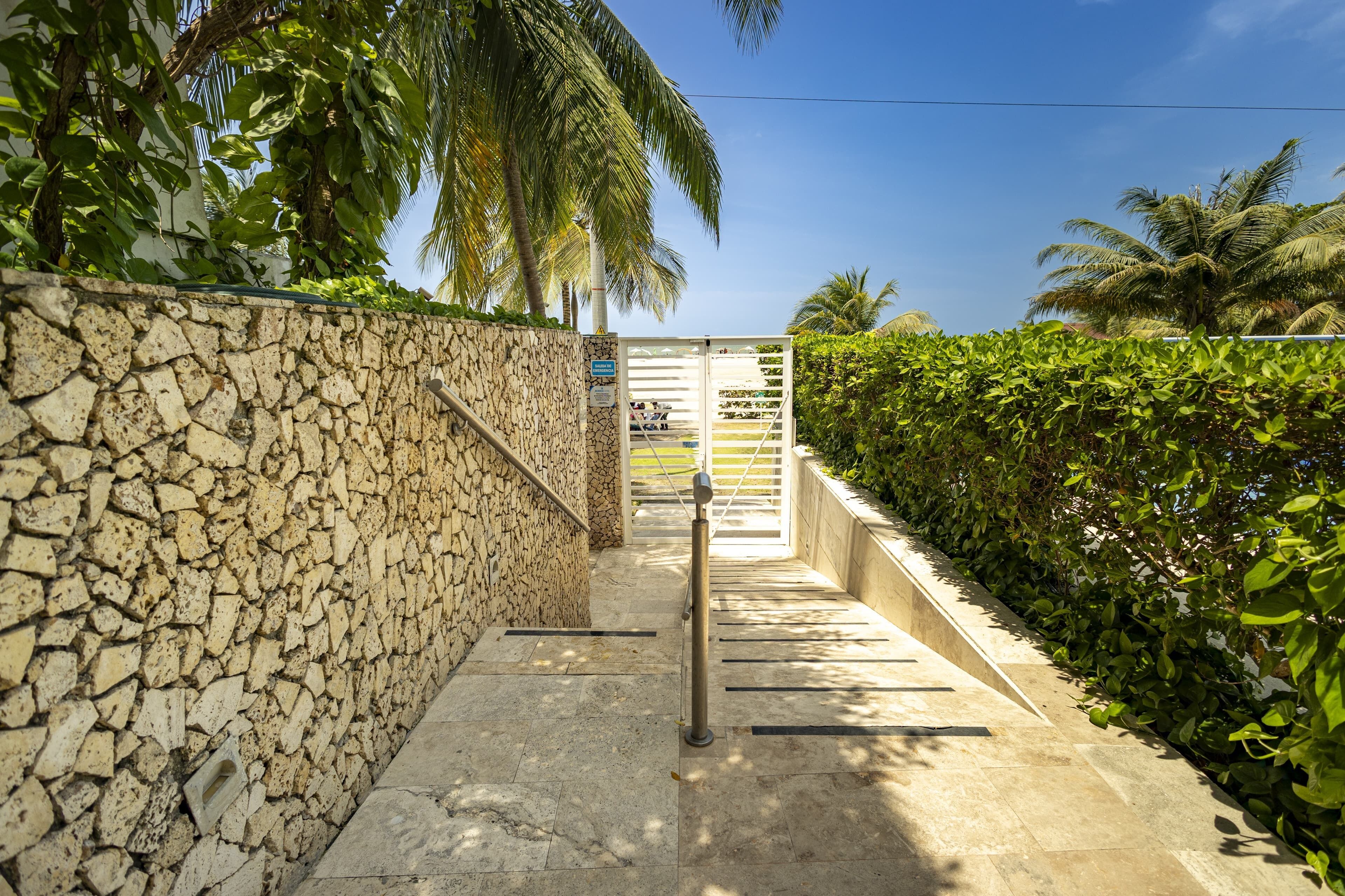 A stone wall with a metal gate leading to a paved area with a metal railing.