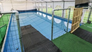 Ein beheiztes Hallenbad mit Fliesenboden, umgeben von einem Metallzaun und einem transparenten Dach.