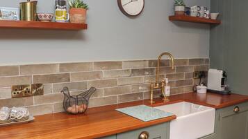 Una cocina con encimera de madera, un fregadero, un reloj y varios utensilios de cocina en estantes.
