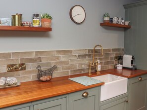 Een keuken met een houten aanrecht, een spoelbak, een klok en diverse keukenbenodigdheden op planken.