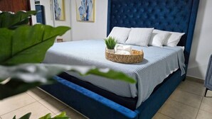 A bed with a blue headboard, white pillows, and a woven basket with a plant and towels. - Luxury stay at a budget friendly cost (San José)
