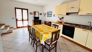 Cocina compacta con comedor, que presenta piso de baldosas, sillas de madera, una mesa con mantel floral, estufa y armarios.