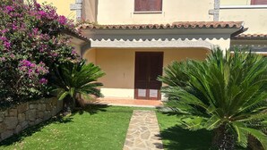 Un patio con un camino de piedra que lleva a un edificio de techo de tejas y contraventanas de madera.