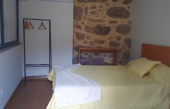 A bedroom with a bed, a wooden headboard, a stone wall, and a metal rack with hangers.