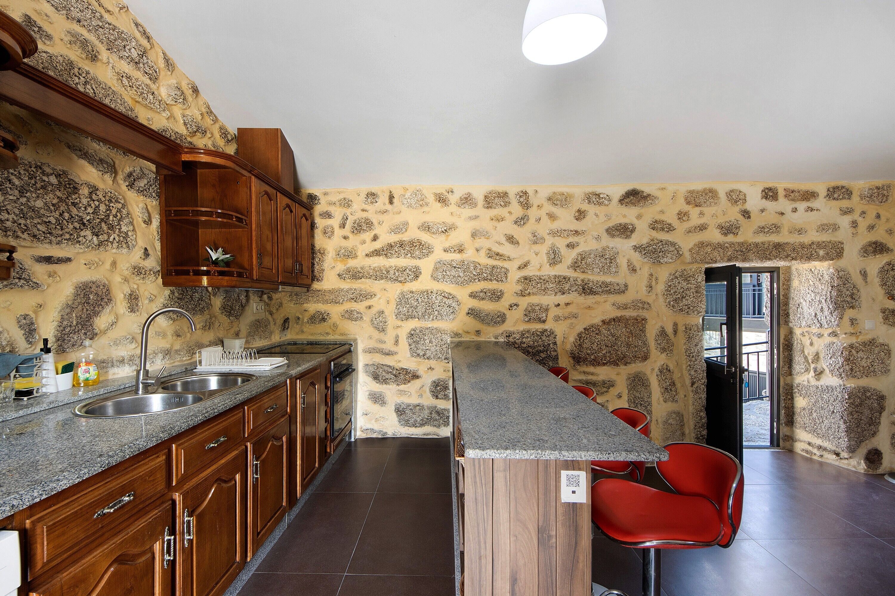 Una cocina con encimeras de granito, armarios de madera, horno empotrado y pared de piedra.